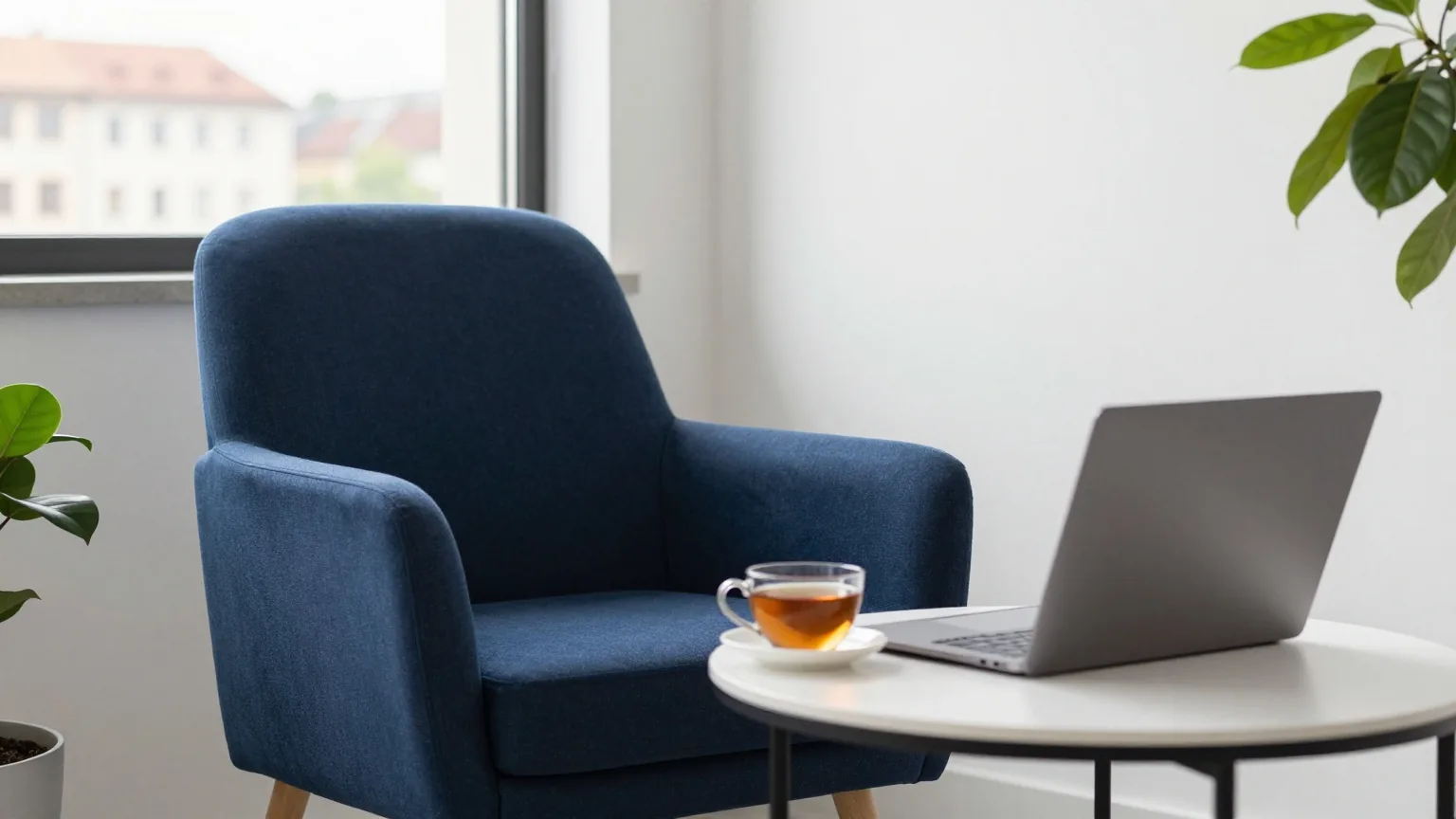 Eine ruhige Leseecke in einem hellen Büro mit Sessel, Beistelltisch, Teetasse und zugeklapptem Laptop
